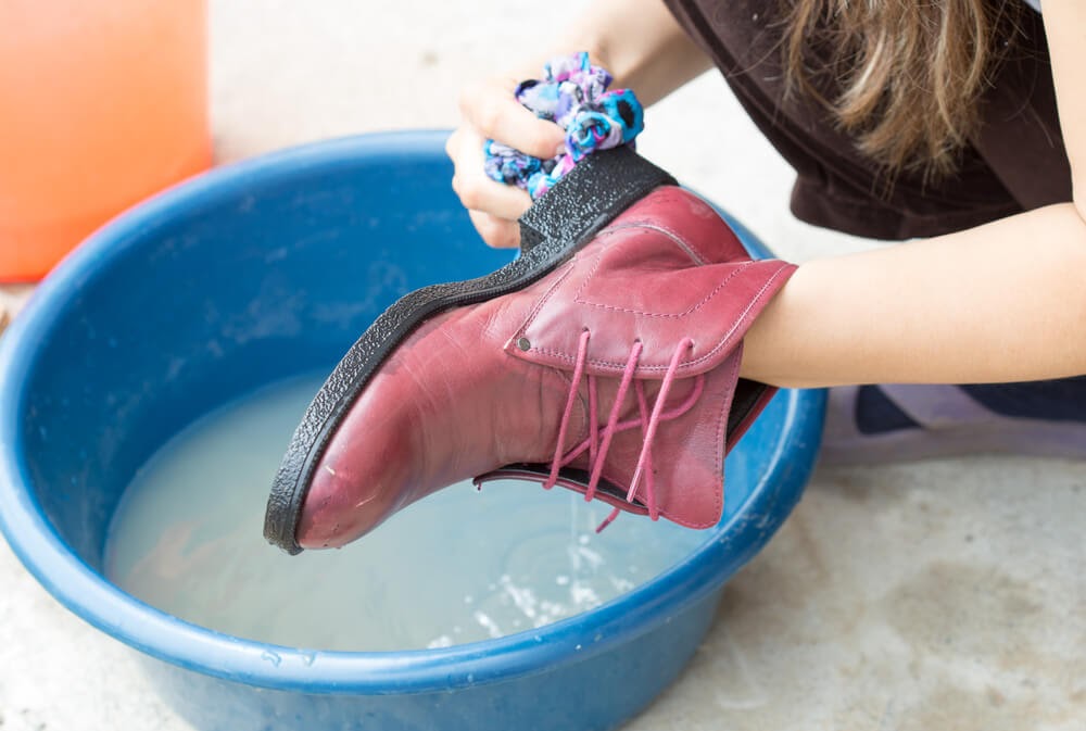 Person scrubbing pink boots in a blue wash basin.