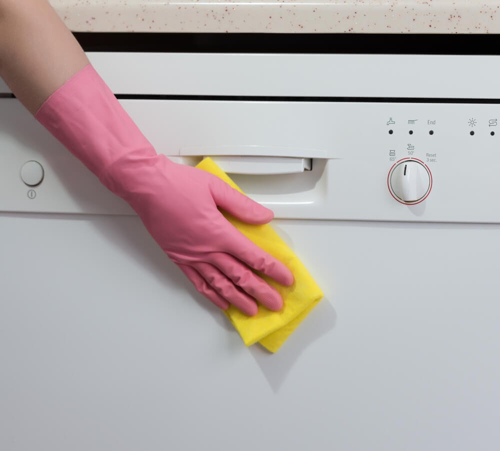 Gloved hand wiping down the front of the dishwasher with a sponge