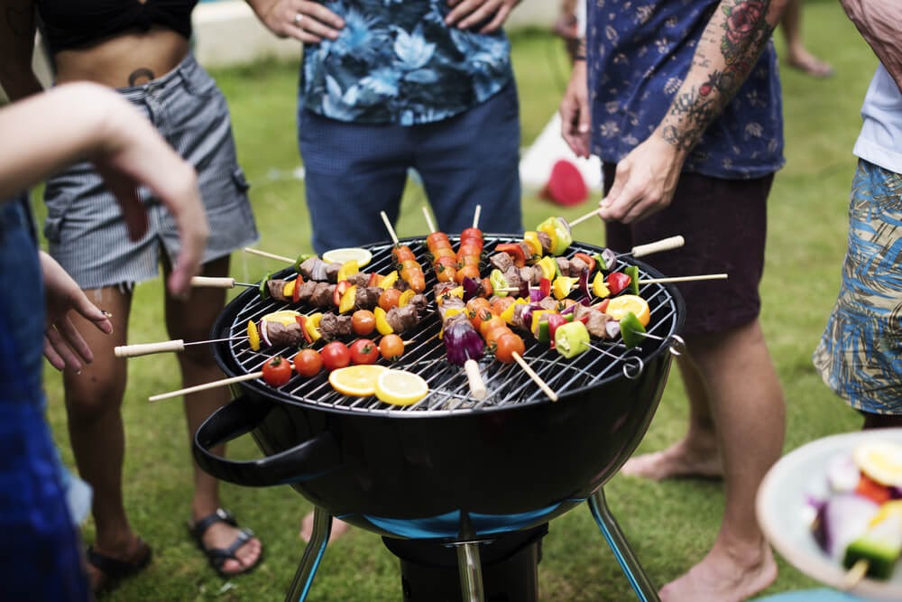 people gathered around a charcoal grill with kabobs