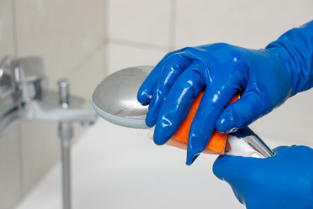 Close up of gloved hand scrubbing a shower head