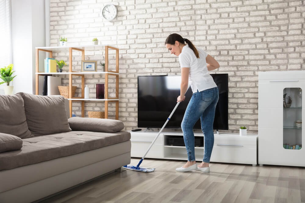 Woman dry mopping hardwood floors with beautiful brick wall in the background