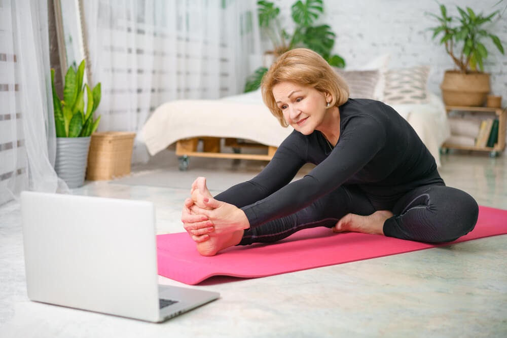 Woman stretched over her yoga mat, looking at her computer
