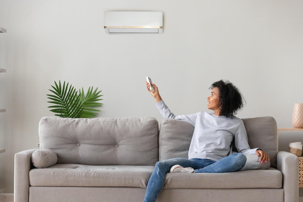 Woman sitting happily on couch as she adjusts her thermostat via a remote