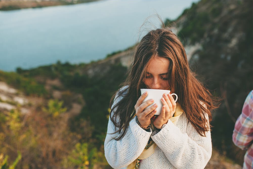 Woman drinking coffee overlooking river.