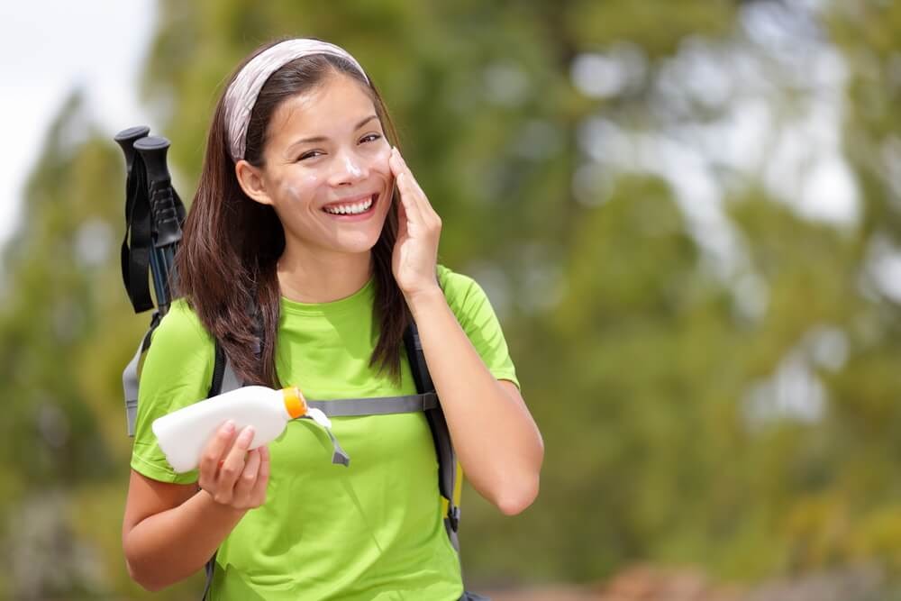 Woman happily putting sunscreen on her face while hiking