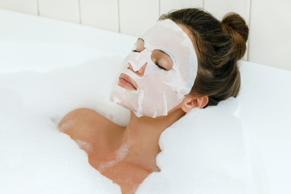 Woman enjoying a bubble bath with a face mask