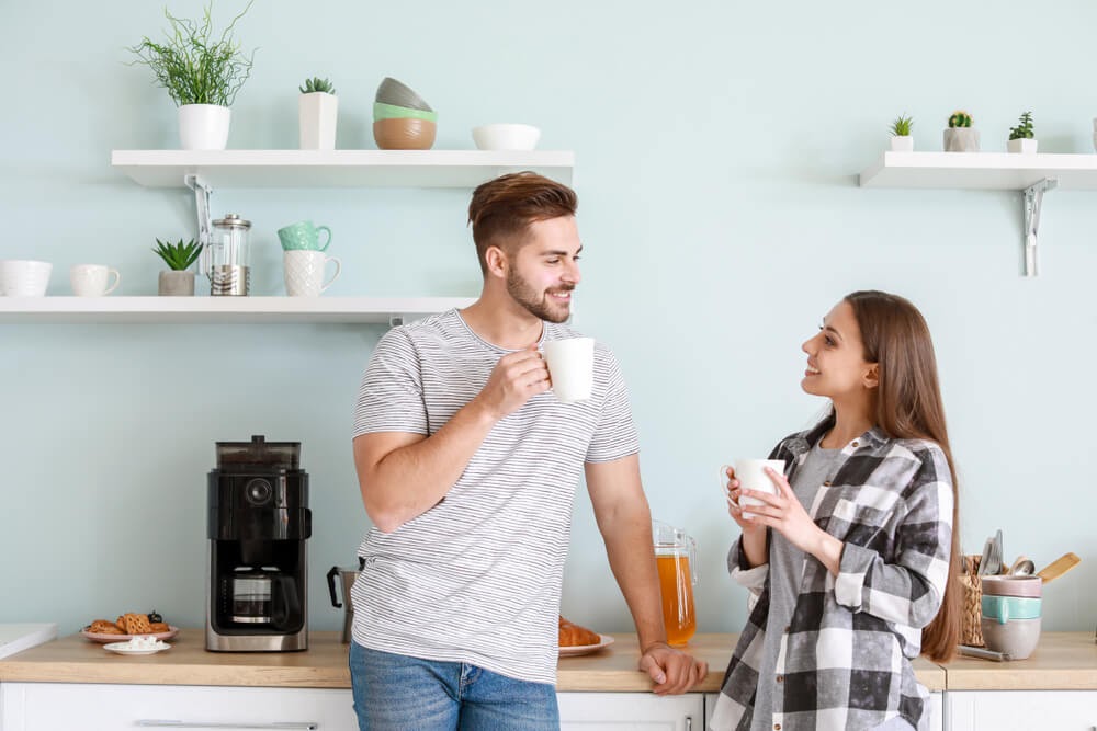 Young couple drinking coffee in light blue kitchen.