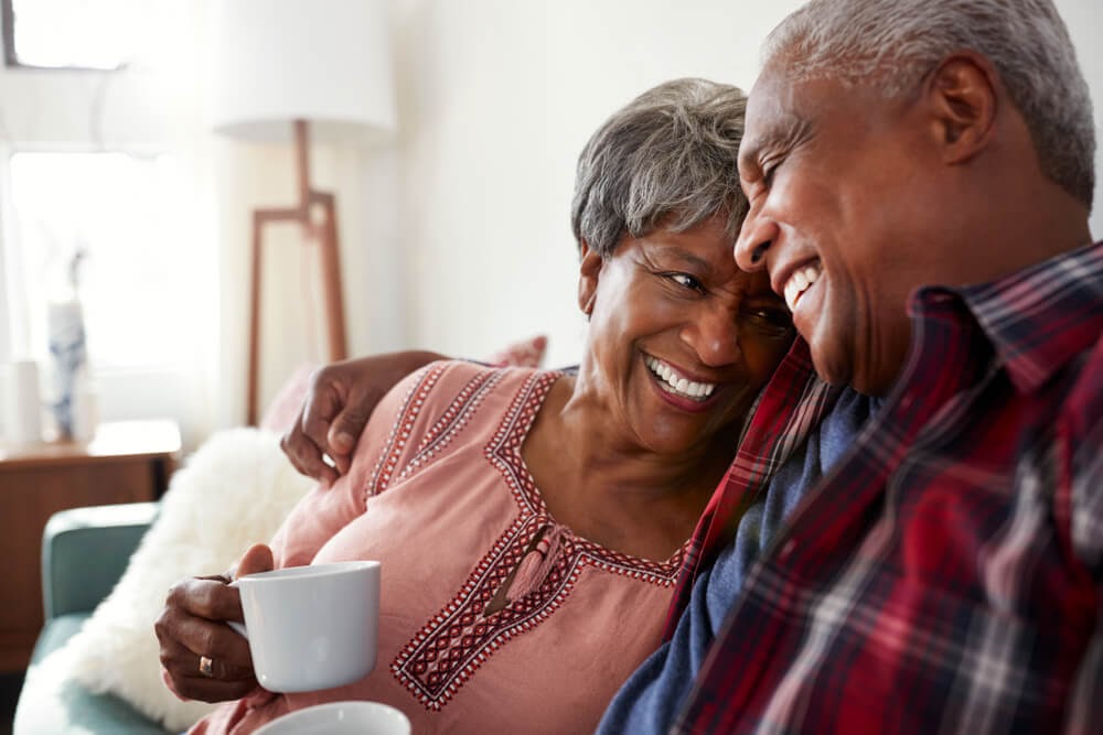 Older couple drinking coffee in living room and laughing.
