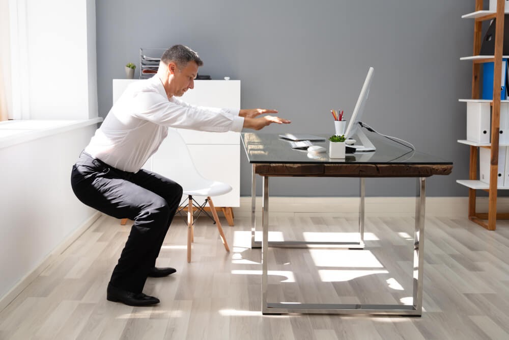 Man doing squats in front of his home desk