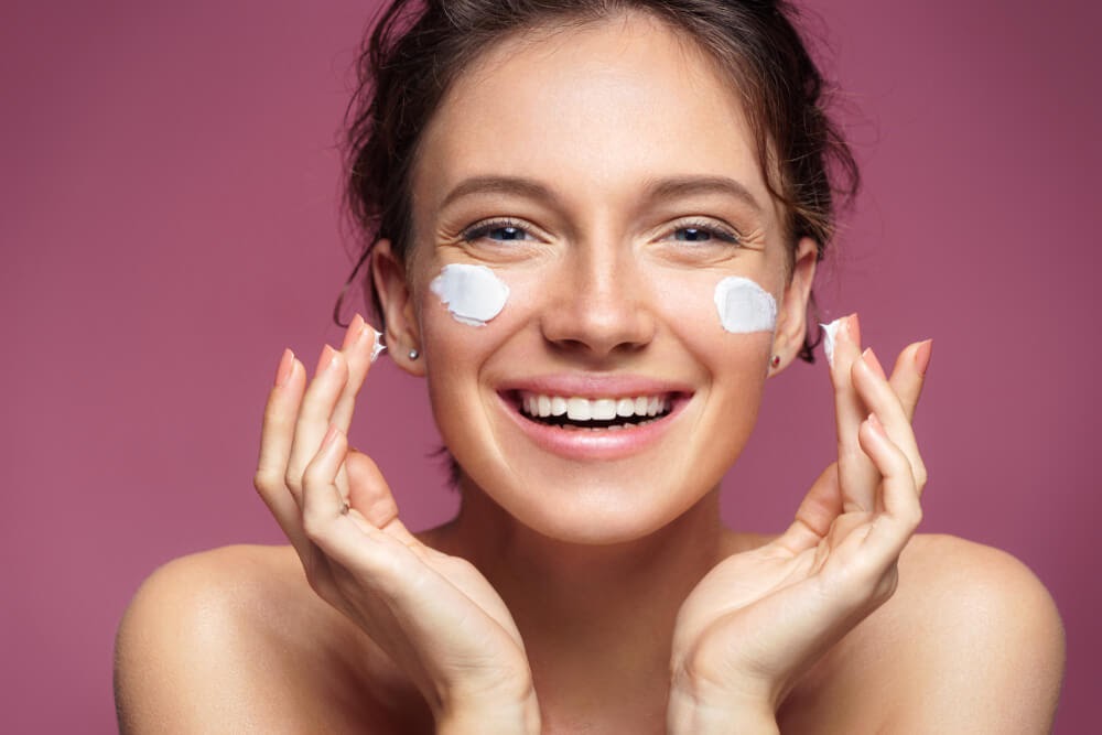 Woman smiling while applying cream to her cheeks