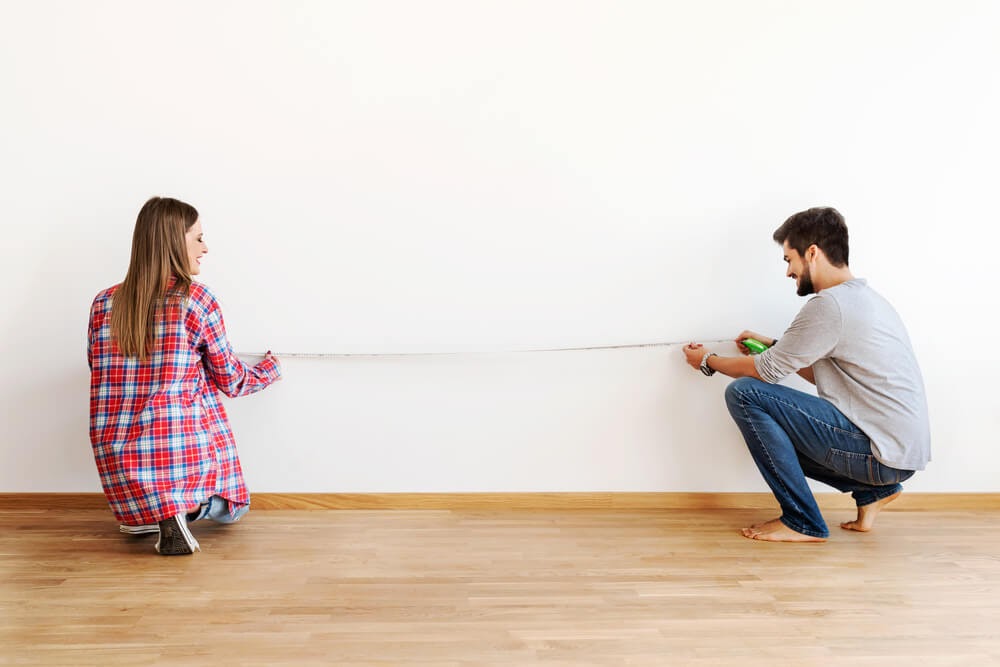Couple measuring their potential couch against the living room wall