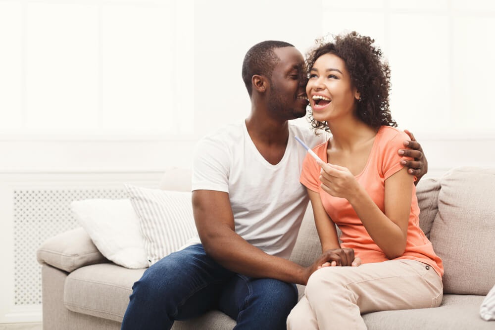 Man and woman canoodling on the couch with a pregnancy test