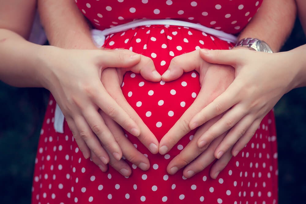 Man and woman making a heart with their hands over a pregnant belly