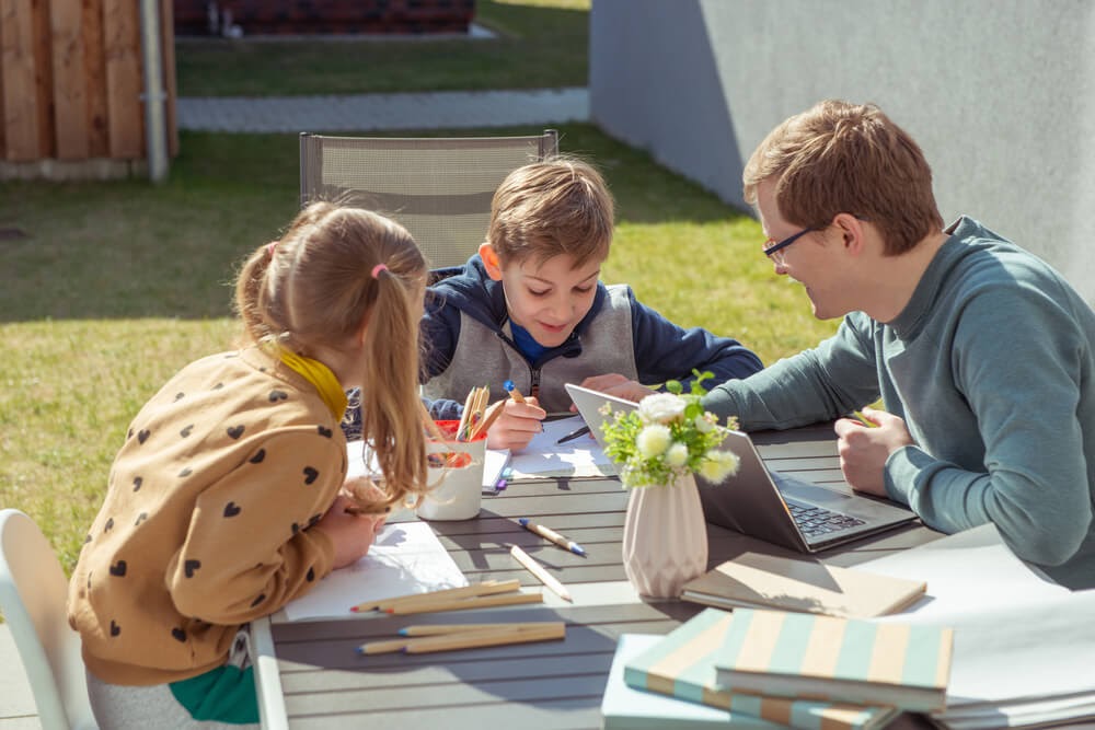 Dad going over schoolwork with his son and daughter in the backyard