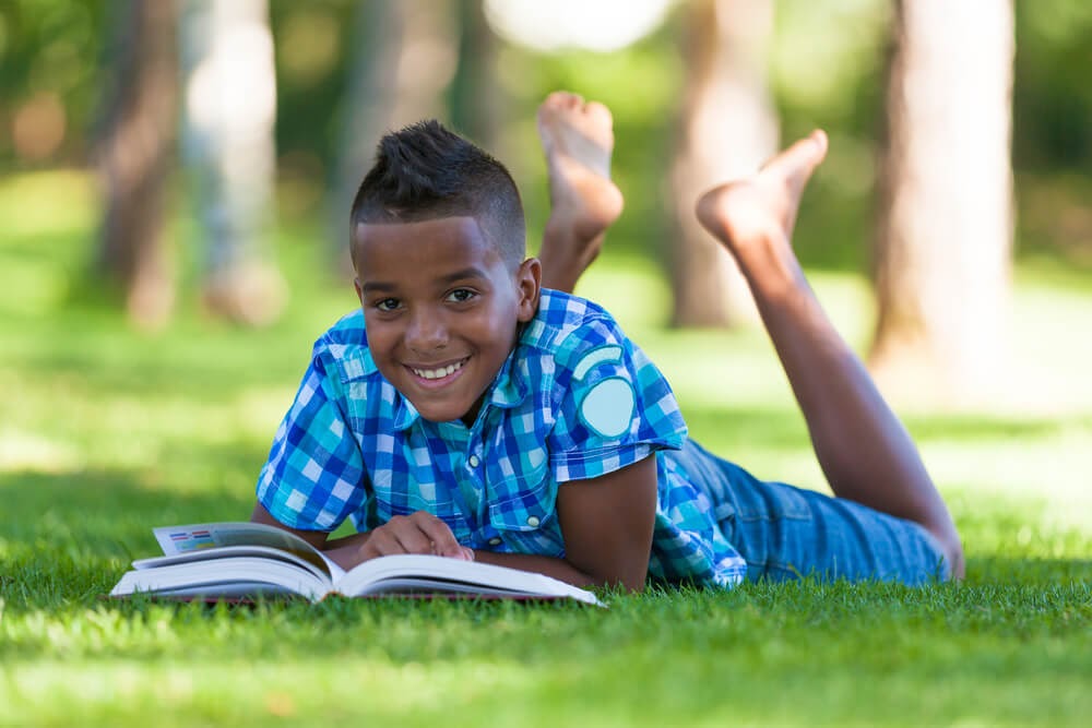 Boy reading in the grass with his feet up in tair