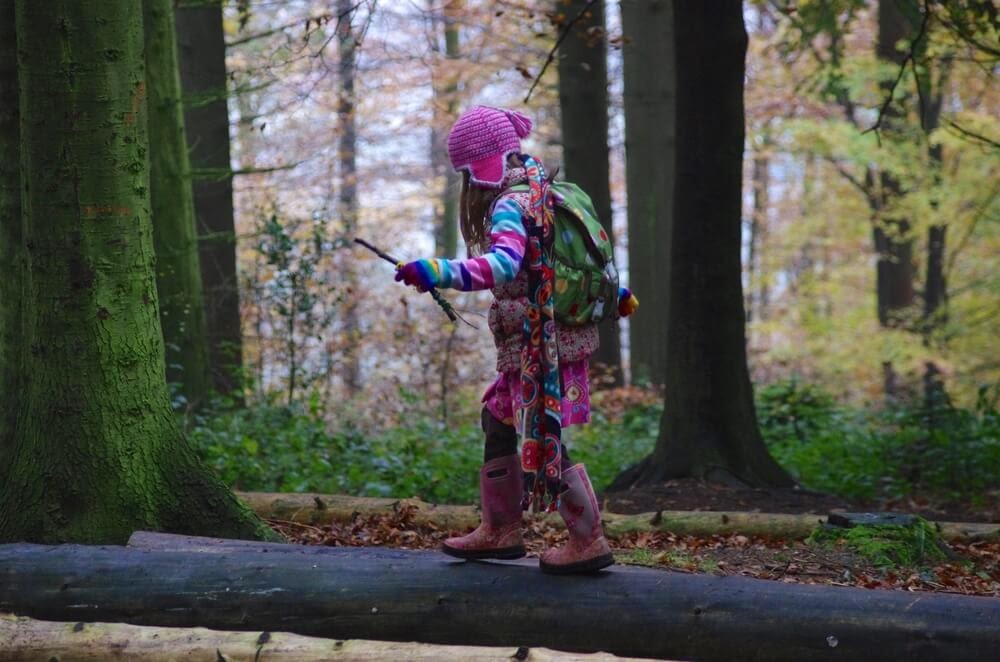 Girl balancing on a grounded tree in her rain gear and backpack