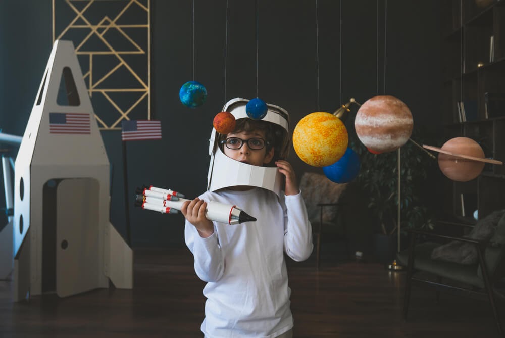 Boy with cardboard astronaut gear and rocket playing space