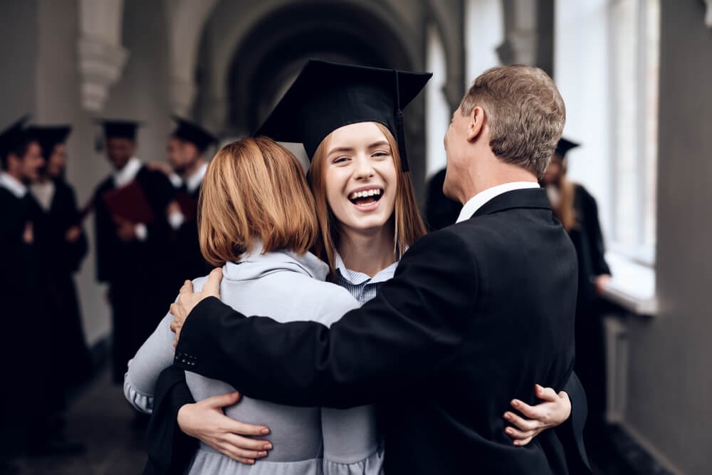 Girl in graduation gear hugging her parents