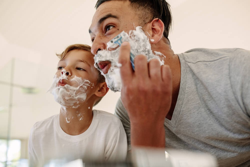Father and son shaving in the mirror
