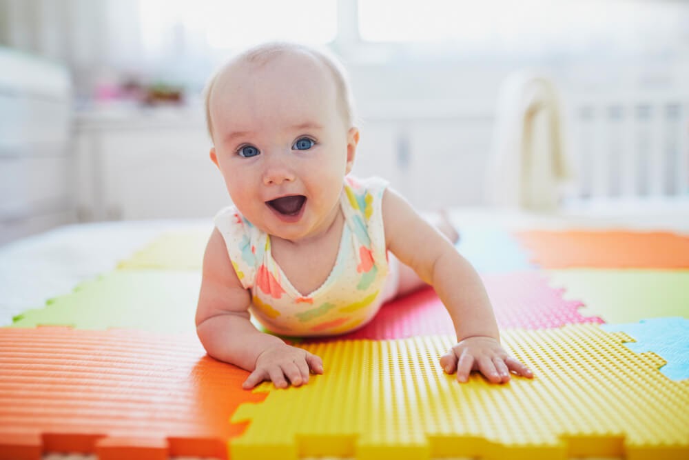 Baby girl on the floor, holding her head up and smiling at the camera