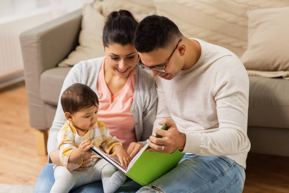 Mom and dad sitting on the floor, reading to their baby