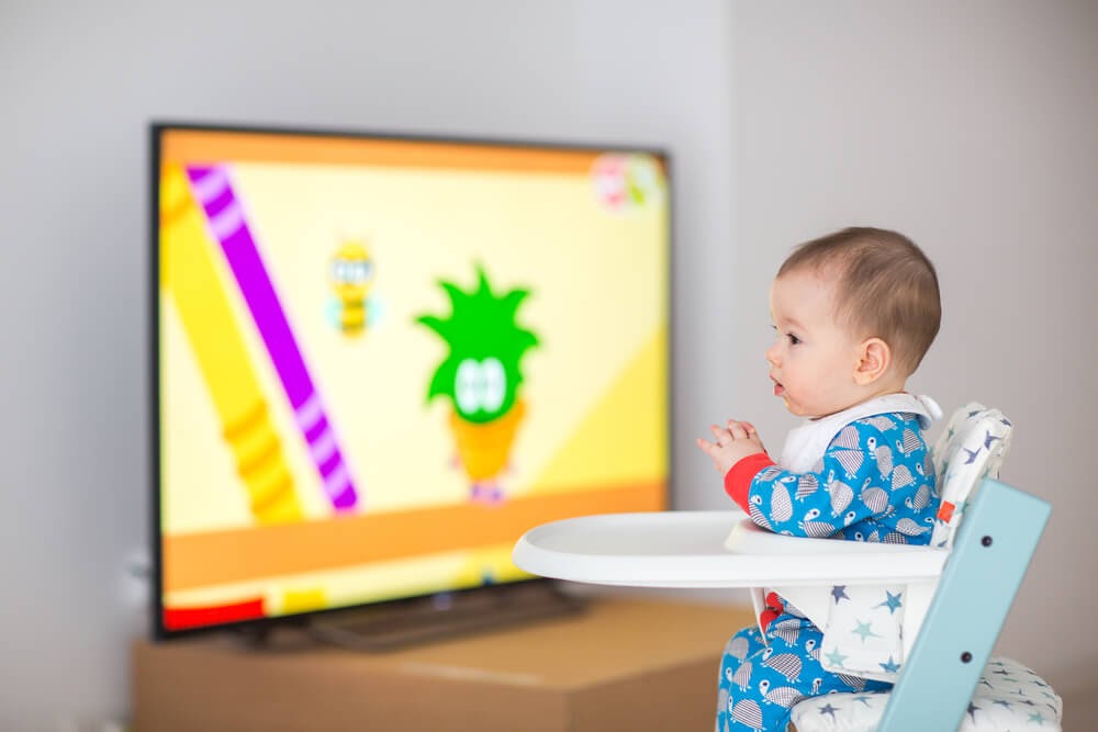 Baby in his highchair with the TV on in the background