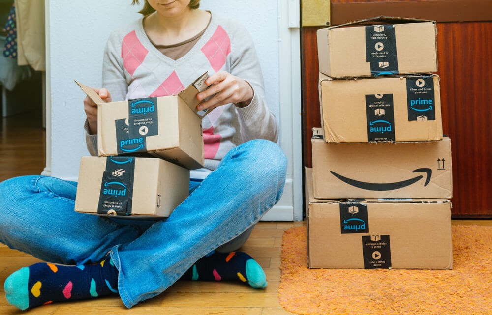 Woman sitting on the ground opening an array of Amazon Prime boxes