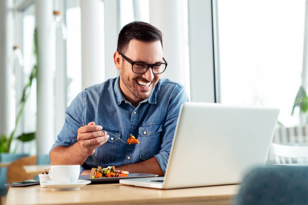 Man eating lunch and laughing with his computer