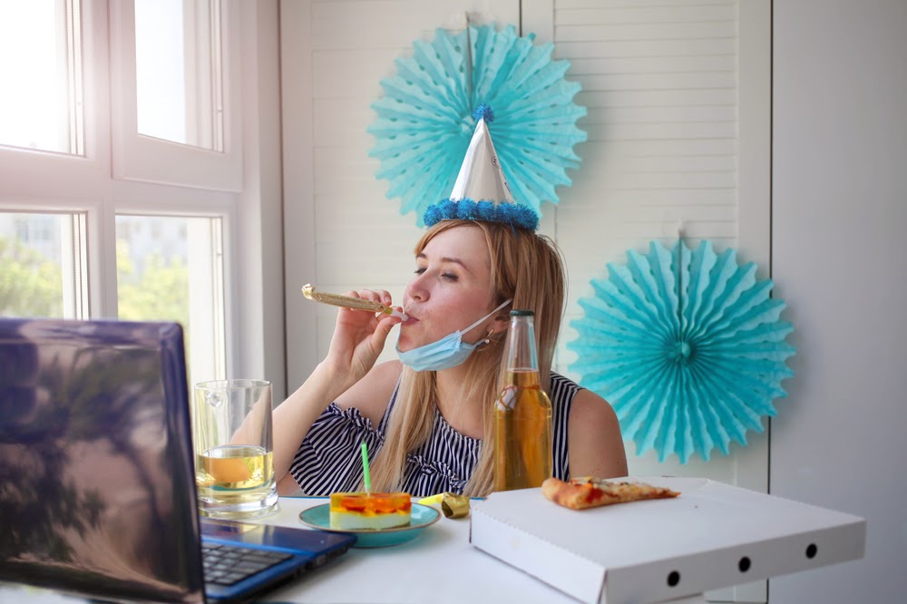 Woman drinking and blowing on a party favor in front of her computer