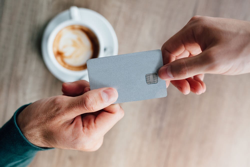 Hand passing credit card to another hand.