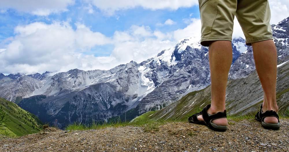 Man in hiking sandals overlooking some snowy mountains in the distance
