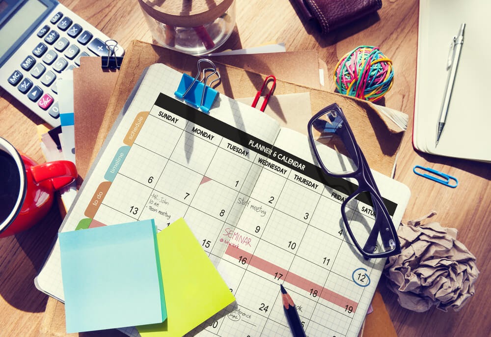 A desk covered in files with a coffee cup and open planner