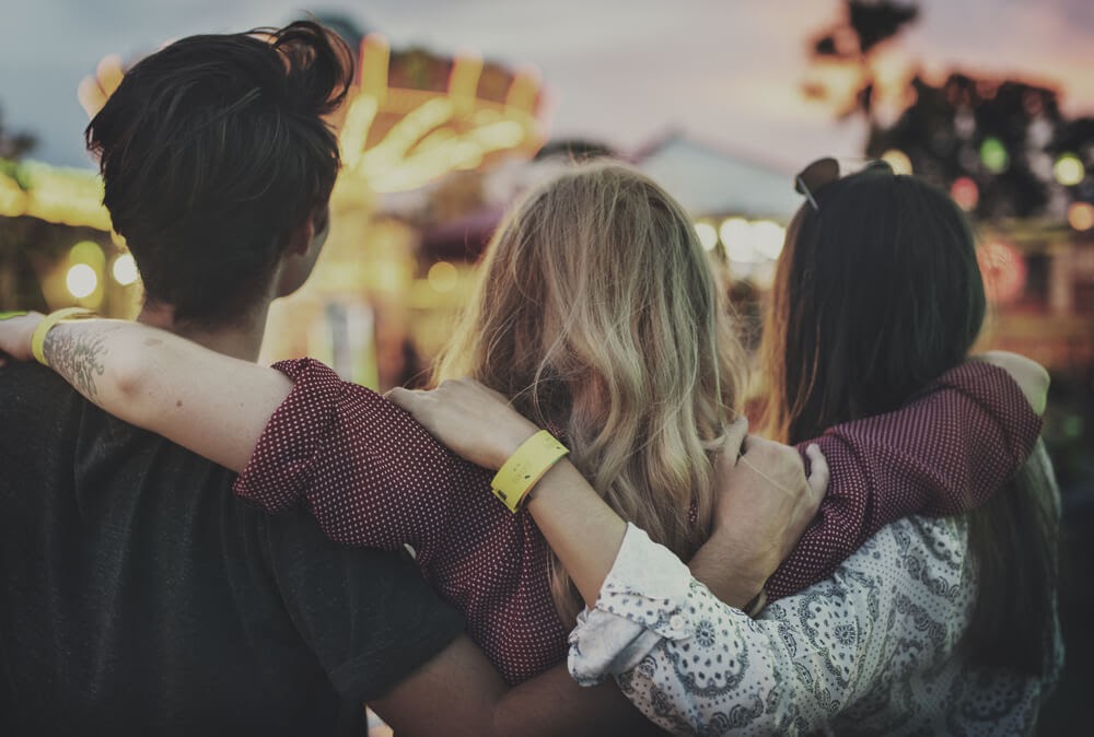 Friends with their arms around each other facing a carnival