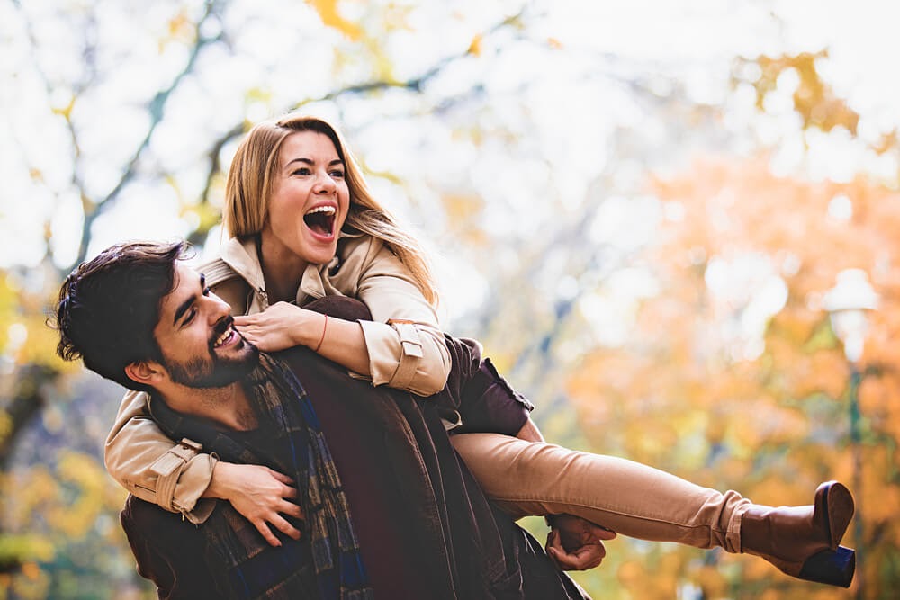 man giving woman a piggy back ride through the park