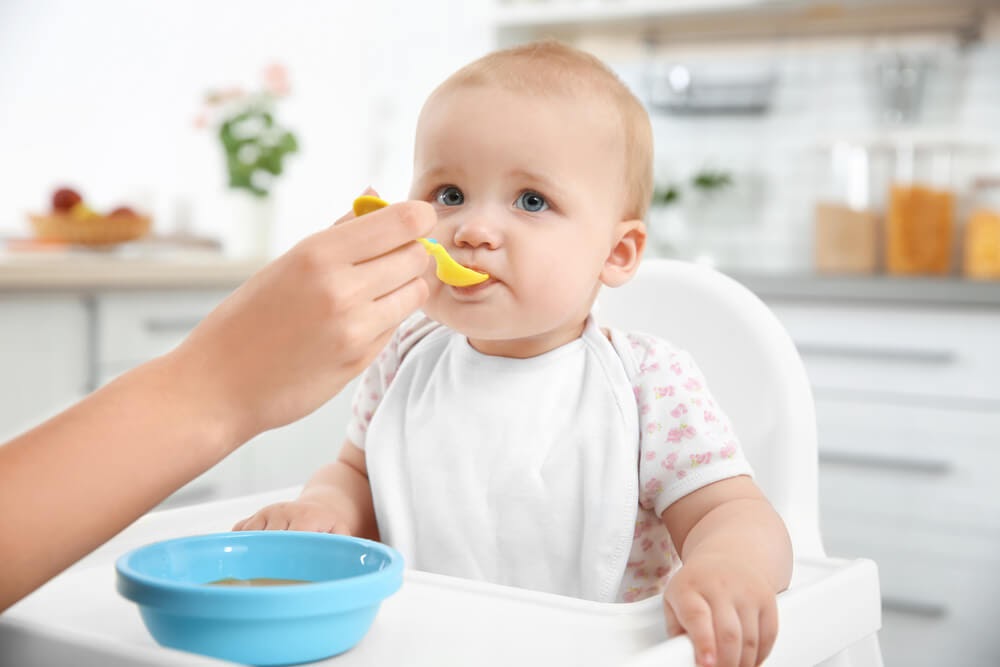 Baby getting spoon fed in high chair