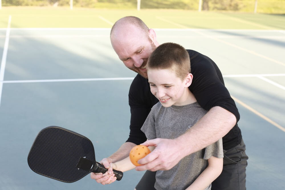 Dad teaching his son how to play pickleball