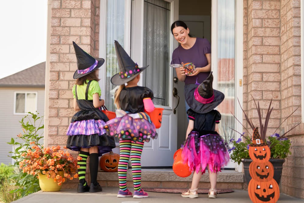 Woman with a bag of candy and three girls dressed up as witches at her door