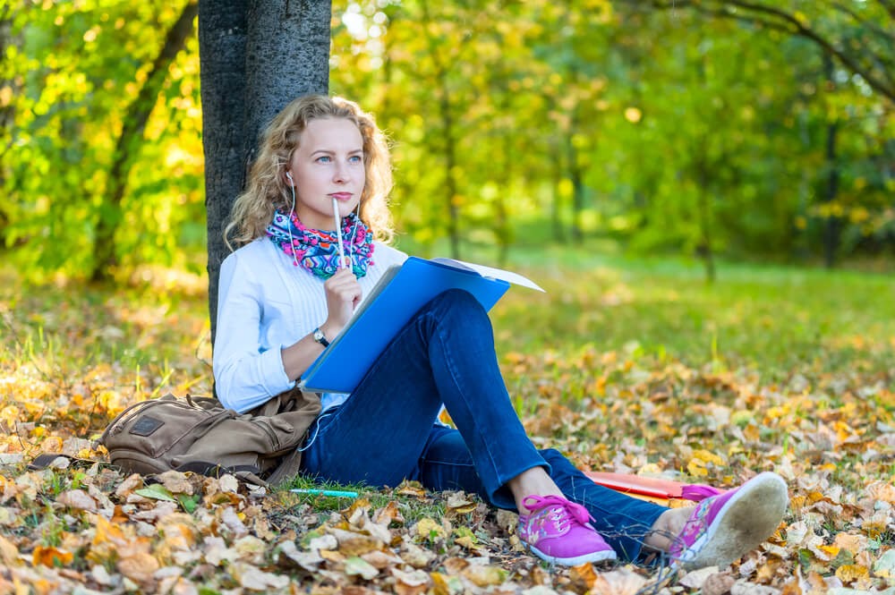Woman leaning next to tree with her notebook, thinking