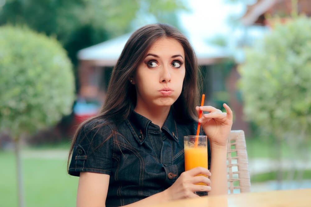 Woman looking uncertain after she takes a drink of orange juice