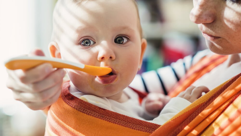 Mom feeding baby while in a baby carrier