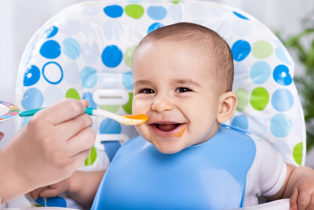 Baby boy smiling in high chair while he eats
