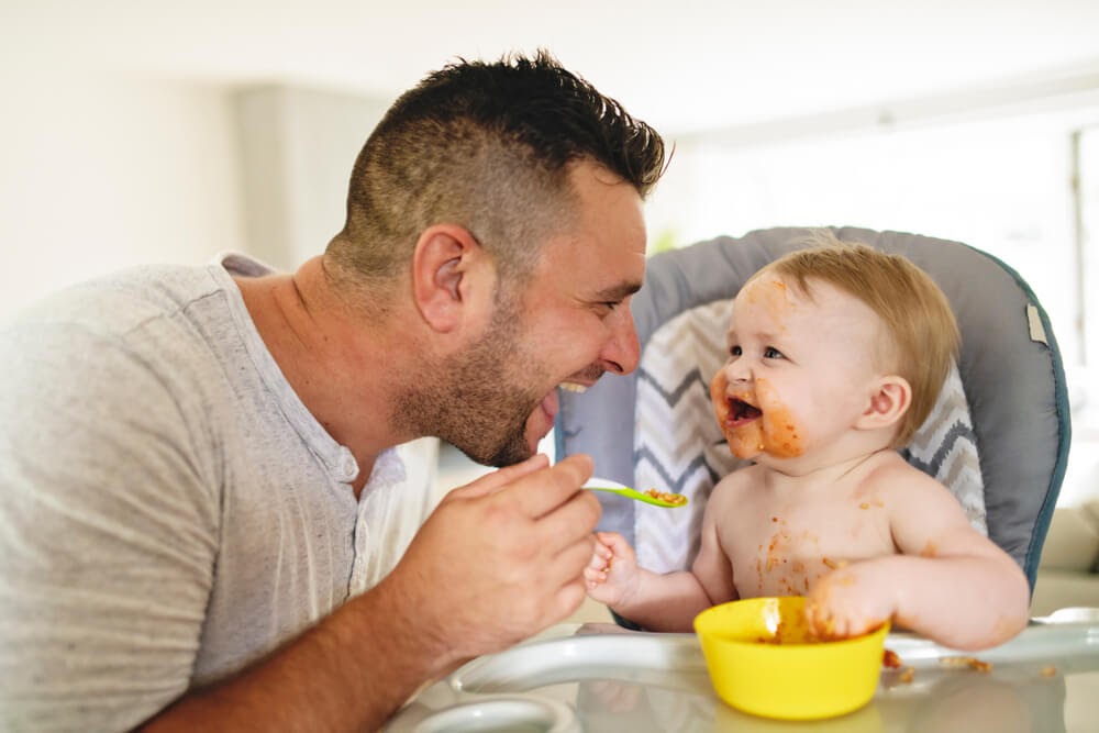 Dad smiling while feeding a messy baby