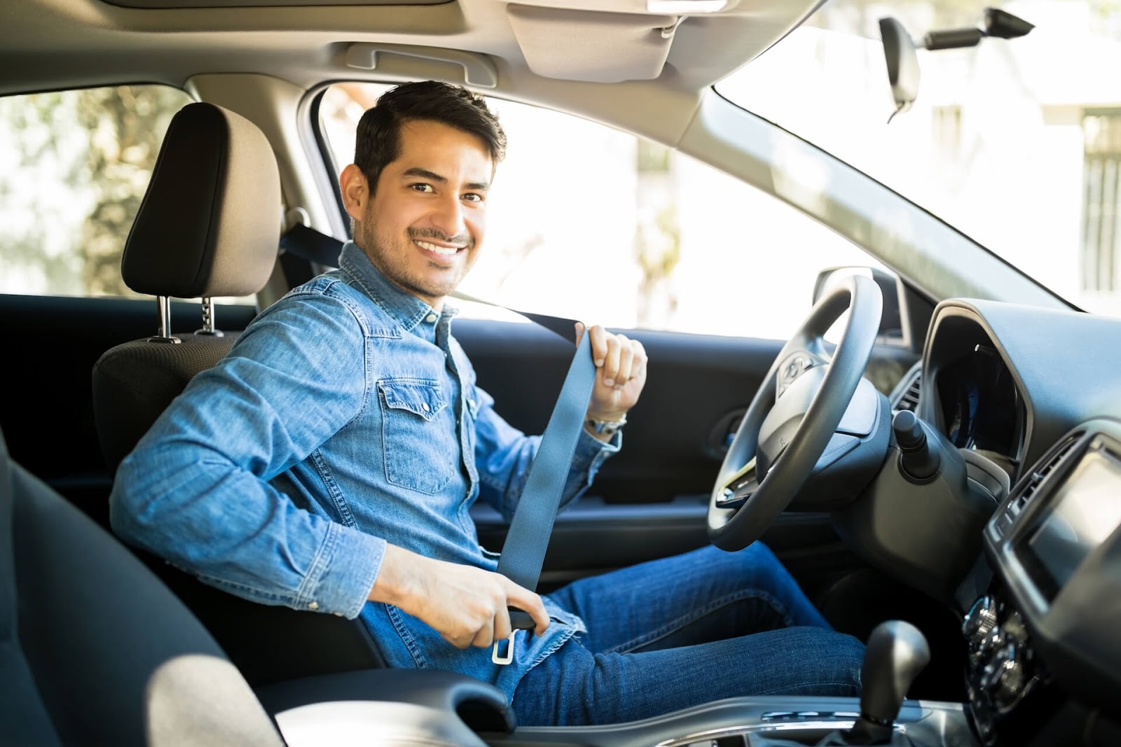 Man smiling at the camera while he puts on his seatbelt