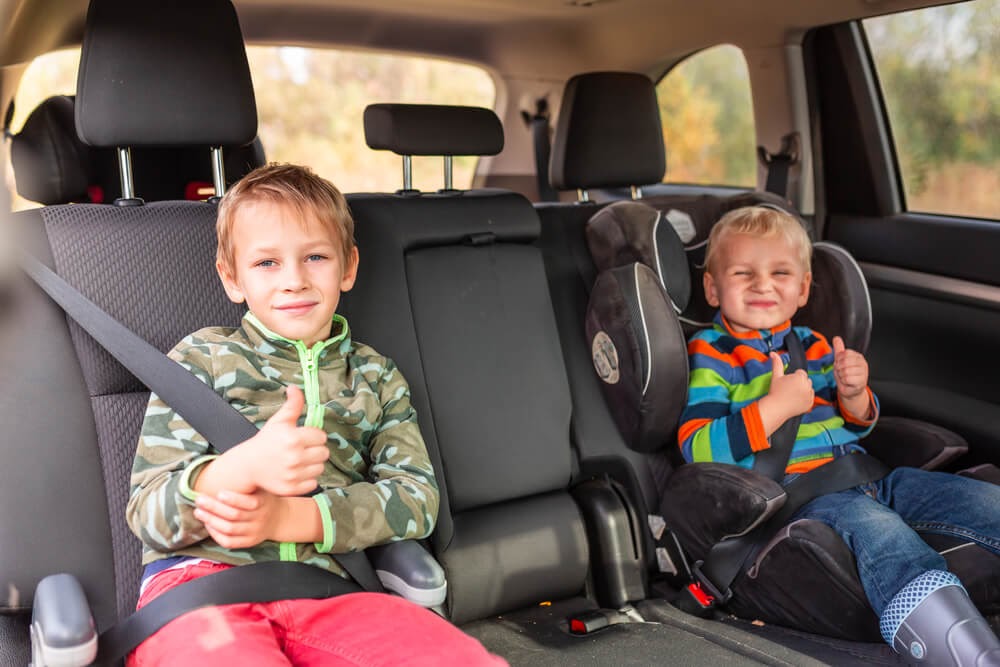 Two brothers giving a thumbs up to the camera from their booster seats