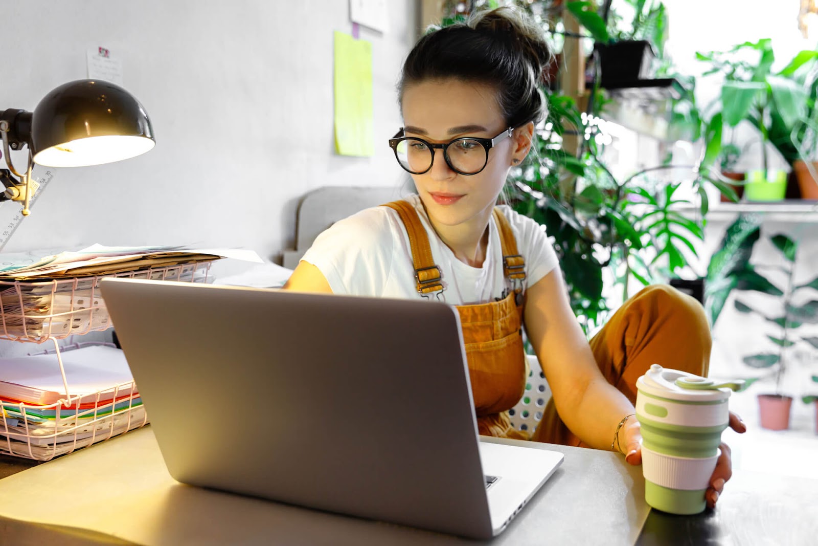 Woman working with coffee in hand and plants in the background