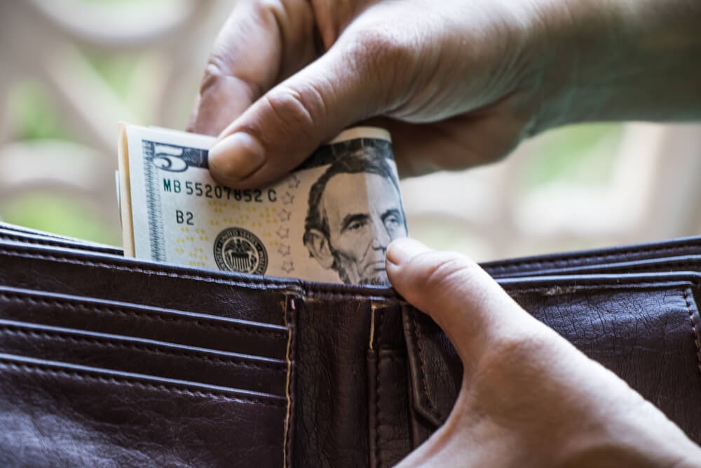Someone pulling out a $5 bill from their wallet