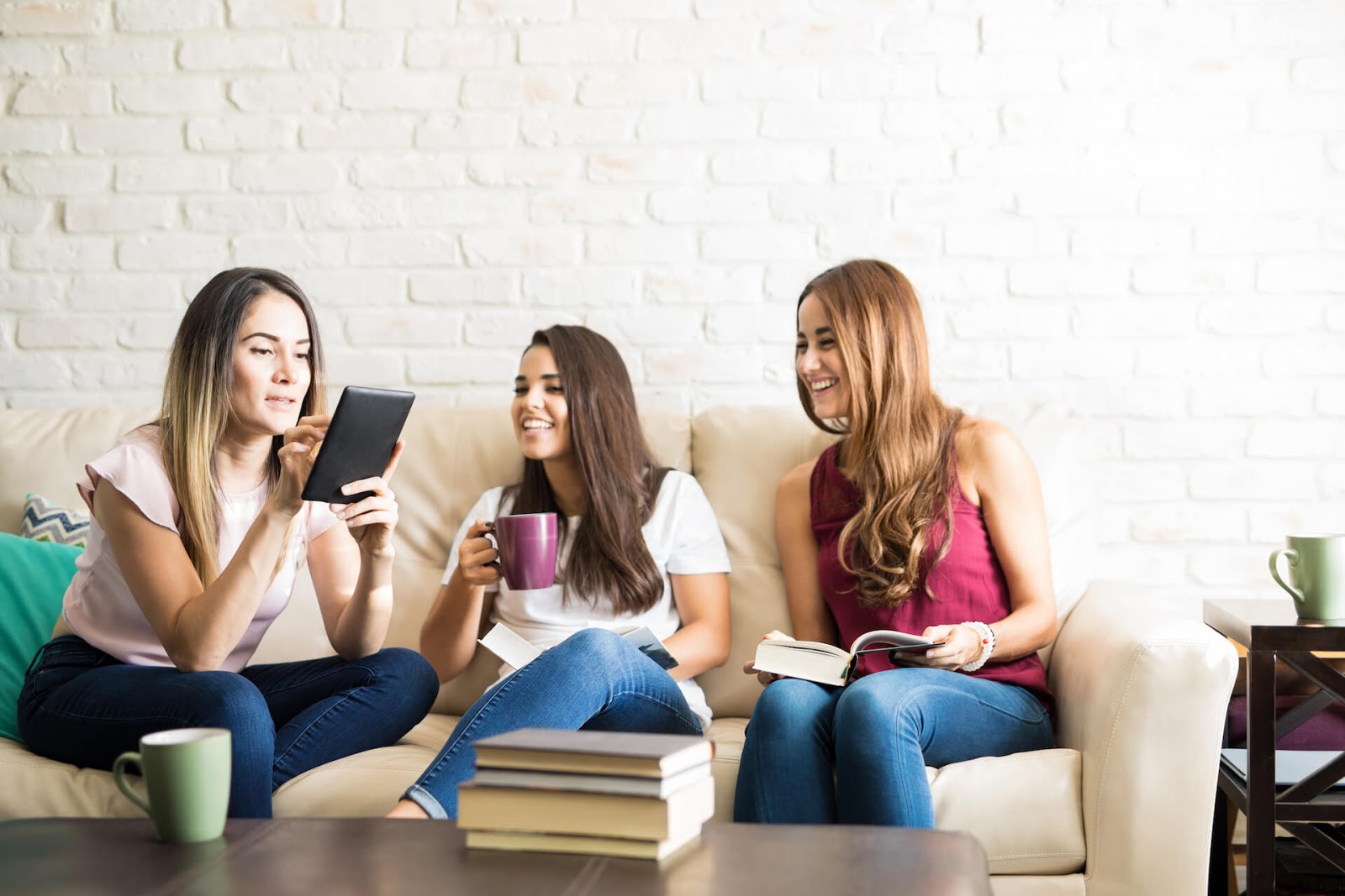 Gals sitting on a couch with books in hand, discussing the novel