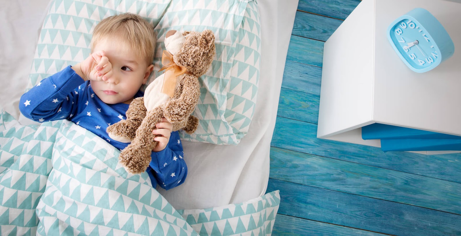 Tired toddler boy rubbing his eyes in bed