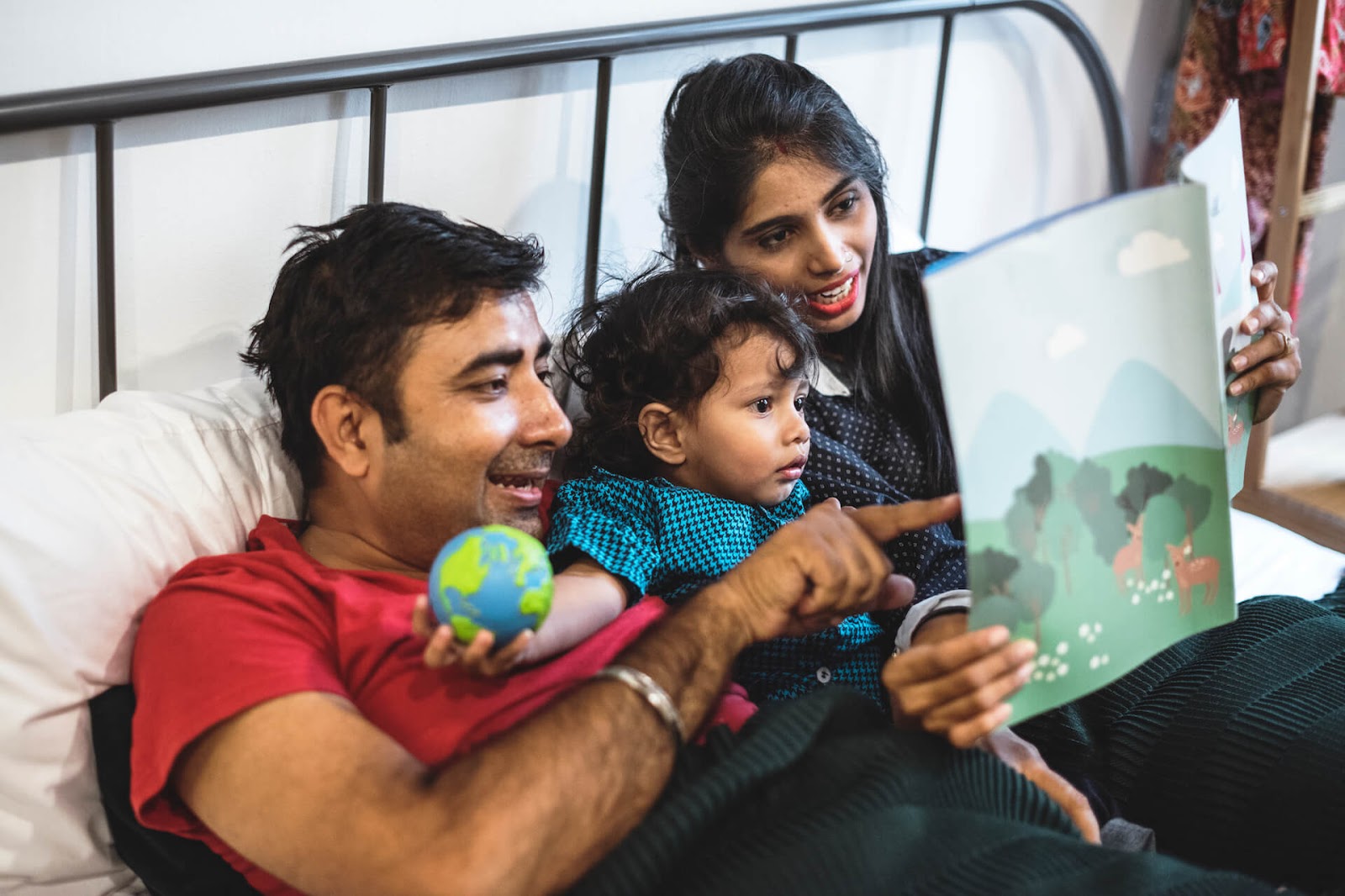 Mom and dad reading to toddler in bed
