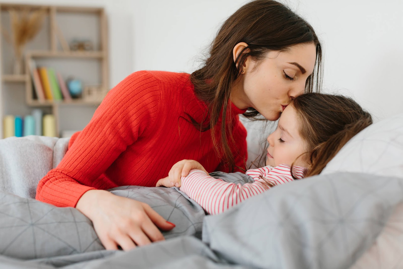 Mom kissing daughter as she tucks her into ed